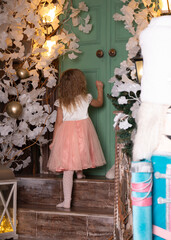 View from the back: a girl in a pink dress stands on the stairs and reaches for the door.