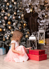 Cute little girl sitting with Christmas gifts under a festive tree, smiling with joy.