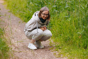 Fototapeta premium Person crouching on a nature path observing plants in a lush green environment during daylight hours