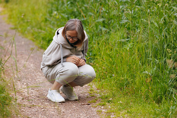 Fototapeta premium Woman crouching near trail observing nature in a lush green environment during a sunny day