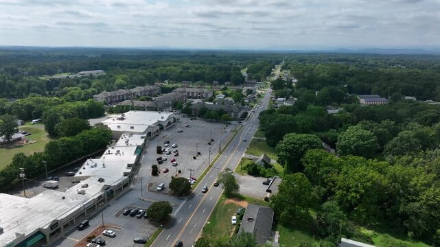 Aerial view of american shopping center stores and townhouses in background. Cloudy summer day with traffic on Main Street in suburbia of Timberlake, Virginia. Wide shot.
