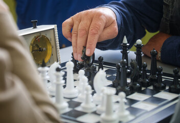 Seasoned grandmaster makes a bold knight move under a ticking chess clock; decisive strategy and deep thought challenge the opponent—business decision metaphor. Photo