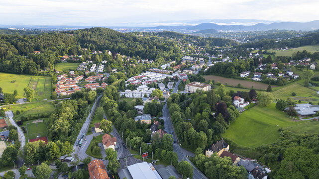 Aerial view of Mariatrost's verdant landscape, where pockets of red-roofed buildings nestle amidst rolling green hills and winding roads, Graz, Styria, Austria.