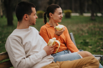 A young couple shares a joyful moment while eating fruit in a peaceful park setting. This wholesome scene captures friendship, connection, and relaxation in a natural outdoor environment.