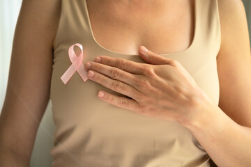 Detailed focus on pink awareness ribbon pinned to shirt with hand touching it, symbolizing support for breast cancer patients during October.