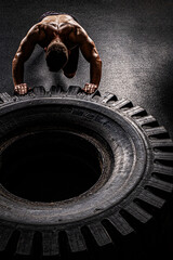 A man with a handsome body pushes a huge wheel. The muscles of the shoulders and back are clearly visible.