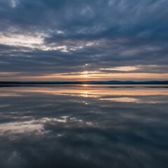 Fototapeta premium Dramatic sunset over calm water reflecting colorful clouds and horizon