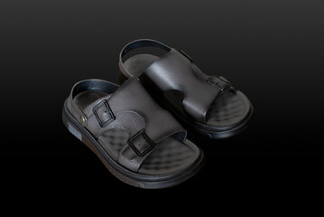 Greyish black leather sandals isolated in black background