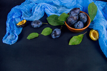 Ripe plums in a clay bowl on a dark background
