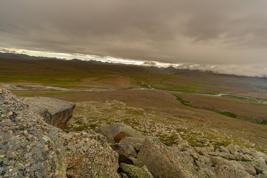 View of a rugged, undulating landscape punctuated by rocky outcrops under a dramatic, cloudy sky, Deosai National Park, Gilgit Baltistan, Pakistan.