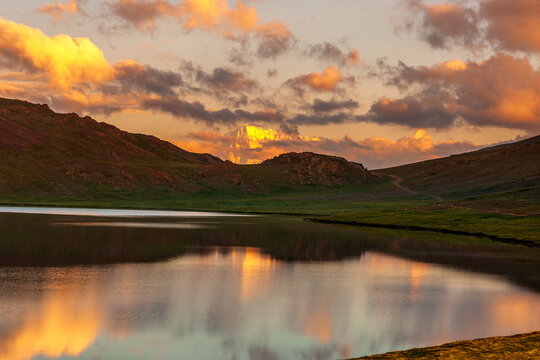 View of placid lake mirroring the fiery sunset and rugged mountains, a serene landscape painting of nature's grandeur, Deosai National Park, Gilgit Baltistan, Pakistan. - Powered by Adobe