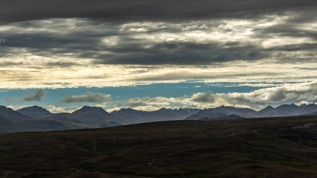 View of a moody landscape with dramatic clouds casting shadows over rolling hills and distant mountains, Deosai National Park, Gilgit Baltistan, Pakistan.