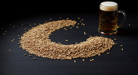 A C-shaped pile of malted barley grains with a mug of amber beer and foam on a dark wooden surface, representing the brewing process