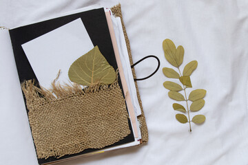 A homemade notebook with a pocket made of burlap, from which a white sheet of paper and a dry leaf...