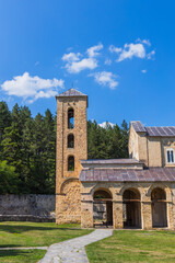 A detailed view of Studenica Monastery&rsquo;s historic stone bell tower and arched portico, featuring a wooden cross under a bright blue sky, ideal for religious, cultural, or heritage storytelling.