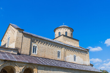 Fototapeta premium Medieval stone monastery dome with cross, arched windows, under a vibrant blue sky, showcasing Byzantine Orthodox Christian heritage and tranquil Eastern European rural landscape. Studenica, Serbia.