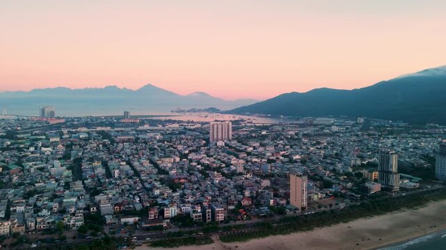 Aerial panorama capturing da nang cityscape merging with coastal waters, son tra peninsula rising behind golden sunset illuminating urban skyline