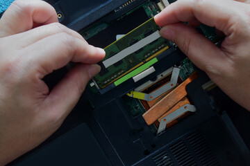 A computer technician repairing the motherboard is installing RAM on a laptop computer on a desk.