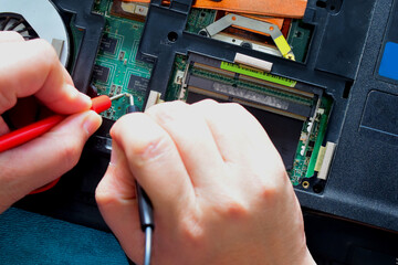 Young computer repairman, laptop motherboard repairman is using IC meter to find faults on motherboard for repair on his desk. Circuit board repair.