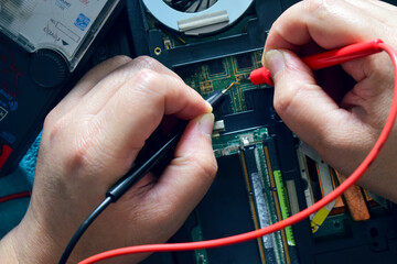 Computer repair technician, laptop motherboard repairman is using IC meter to find faults on motherboard for repair on his desk. Circuit board repair with modern technology.