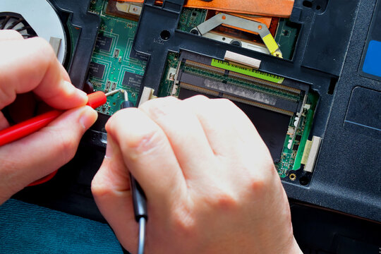 Young computer repairman, laptop motherboard repairman is using IC meter to find faults on motherboard for repair on his desk. Circuit board repair.