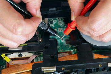 Young computer repairman, laptop motherboard repairman is using IC meter to find faults on motherboard for repair on his desk. Circuit board repair.