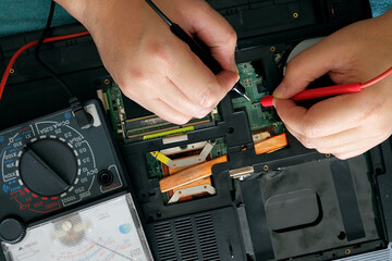 Young computer repairman, laptop motherboard repairman is using IC meter to find faults on motherboard for repair on his desk. Circuit board repair.