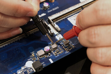 Young computer repairman, laptop motherboard repairman is using IC meter to find faults on motherboard for repair on his desk. Circuit board repair.