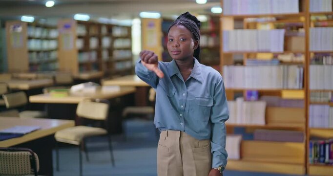 African young adult gen z upset lady female look camera show thumbs down finger hand sign. Teen pupil sad alone girl staring cam fail exam study bad result inside college place