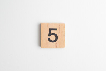 Single wooden block with the number "5" printed in black on a white isolated background. Educational toy for children learning numbers or for creative design and math concepts.