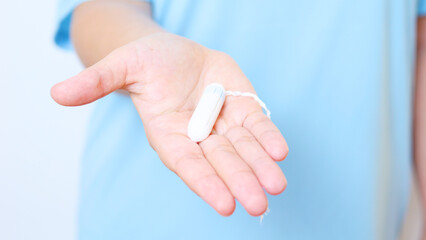 Woman holding tampon, representing feminine hygiene needs during menstrual cycle. Soft blue...