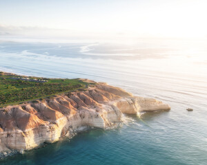 Aerial view of rugged cliffs meet the azure sea, bathed in the golden light of dawn along the coastline, Port Willunga, South Australia, Australia.