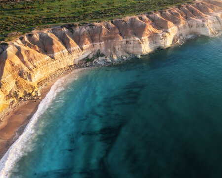 Aerial view of golden cliffs meet the turquoise sea, a symphony of earth and water, where time stands still on the sands of the shore, Port Willunga, South Australia, Australia.