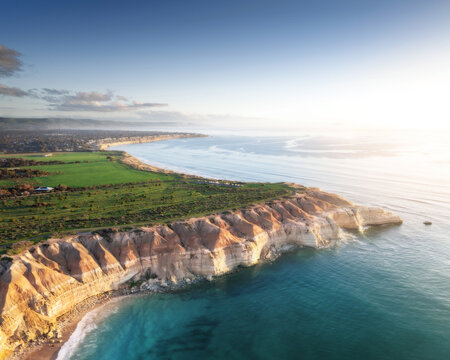 Aerial view of rugged cliffs meet the turquoise sea in a dance of sunlight and shadow, painting a vivid coastal panorama., Port Willunga, South Australia, Australia.