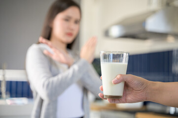 Allergy dairy food lactose intolerance allergen health care illness concept. Selective focus on a glass of milk with blurred woman gesturing refusing stop or reject say no to cow milk.
