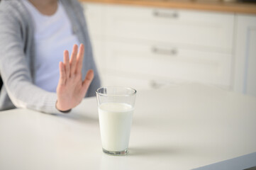 Allergy dairy food lactose intolerance allergen health care illness concept. Selective focus on a glass of milk with blurred woman gesturing refusing stop or reject say no to cow milk.