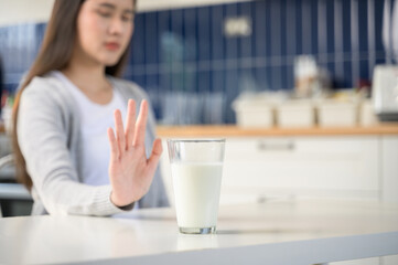 Allergy dairy food lactose intolerance allergen health care illness concept. Selective focus on a glass of milk with blurred woman gesturing refusing stop or reject say no to cow milk.