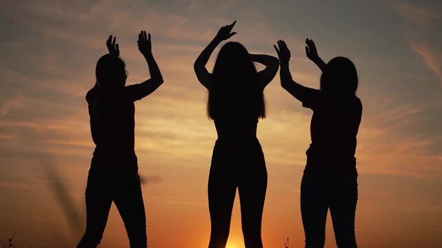 Dancing silhouette trio at sunset show three woman raising arms against glowing orange sky and horizon during soft dusk capturing friend bond and group movement in silhouette sunset silhouette repeat