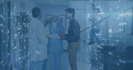 Healthcare team discussing patient documents in hospital corridor, with stethoscopes and folder