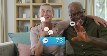 Smiling senior Black man and woman in pink blouse sitting on sofa, showing chat bubble 73