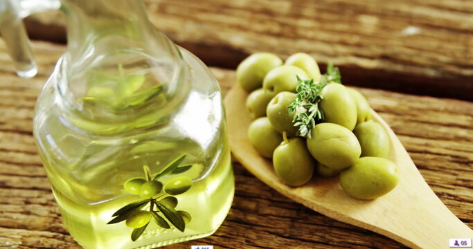 Fototapeta Showing glass bottle of olive oil on weathered table, spoon holding olives, herb sprig, copy space