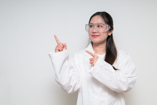 Asian healthcare worker scientist woman in lab coat with safety goggle glasses pointing finger up - Powered by Adobe