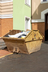 Yellow industrial dumpster with construction debris near modern residential building.