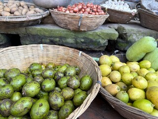 Rustic baskets overflow with fresh green ambarella fruits, light lemons, garlic, onions, and potatoes