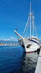 Fototapeta premium A white boat with sails docked in a harbor on a sunny day with a clear blue sky
