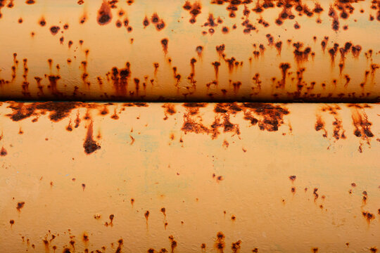 A close-up shot of two rusted yellow metal pipes with a thick layer of peeling paint, creating an industrial and grunge-like textur