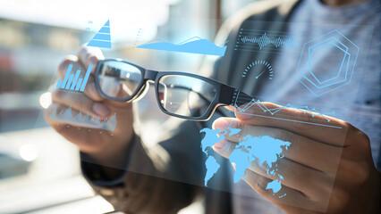 Businessman holding eyeglasses with futuristic data visualization interface, showing charts, graphs, world map, and analytics dashboard, symbolizing business intelligence, data analysis, and digital t