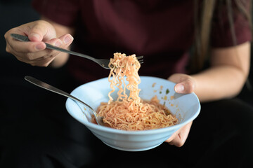 Close-up of Asian woman sitting at home in sofa eating instant noodles from bowl