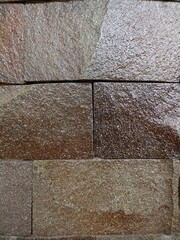 Close-up of a wet, textured stone wall with varying shades of brown, showcasing a natural and rustic pattern.