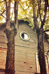 Old wooden house with a round attic window framed by autumn trees with golden leaves, retro tones processing, countryside autumn landscape